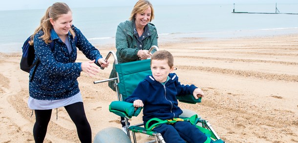 Two smiling women pushing a young boy in a wheelchair on a beach