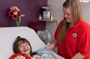 Young female carer stood next to a smiling girl in a hospital bed