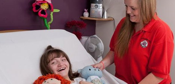 Young female carer stood next to a smiling girl in a hospital bed