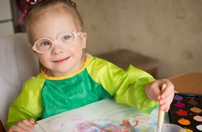 Young girl wearing glasses painting a picture at a table