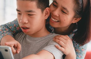 Young disabled boy looking at laptop with mum leaning over his shoulder pointing and smiling