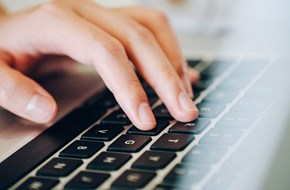 Close-up image of a hand typing on a laptop keyboard