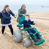 Two smiling women pushing a young boy in a wheelchair on a beach